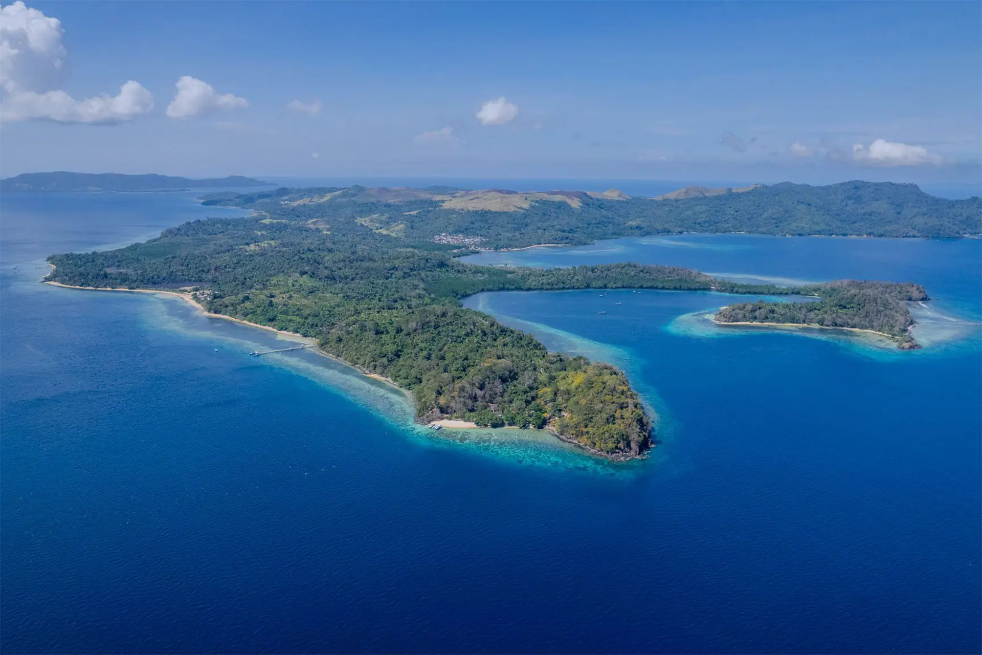 Aerial view of North Sulawesi Indonesia coastline with lush tropical jungle, white sand beaches, and vibrant coral reef waters — Columbus Scuba dive trip