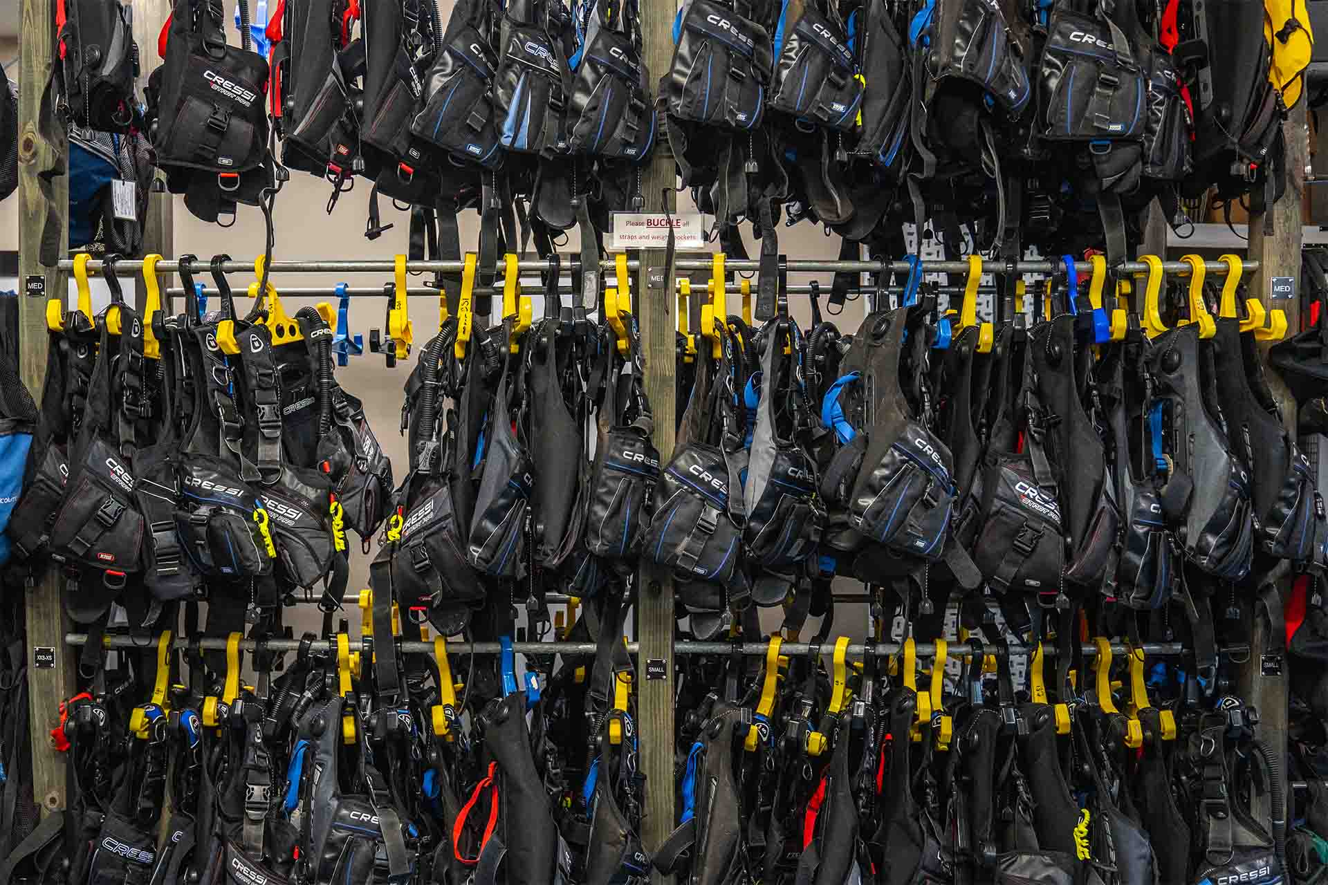 Rental BCDs organized on wall storage racks at Columbus Scuba rental gear room
